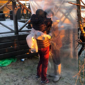 Two persons outdoors hugging through a plastic sheet. Photo.